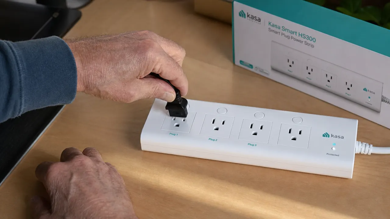 Hand plugging a monitor cord into one of the six outlets on the Kasa HS300 power strip