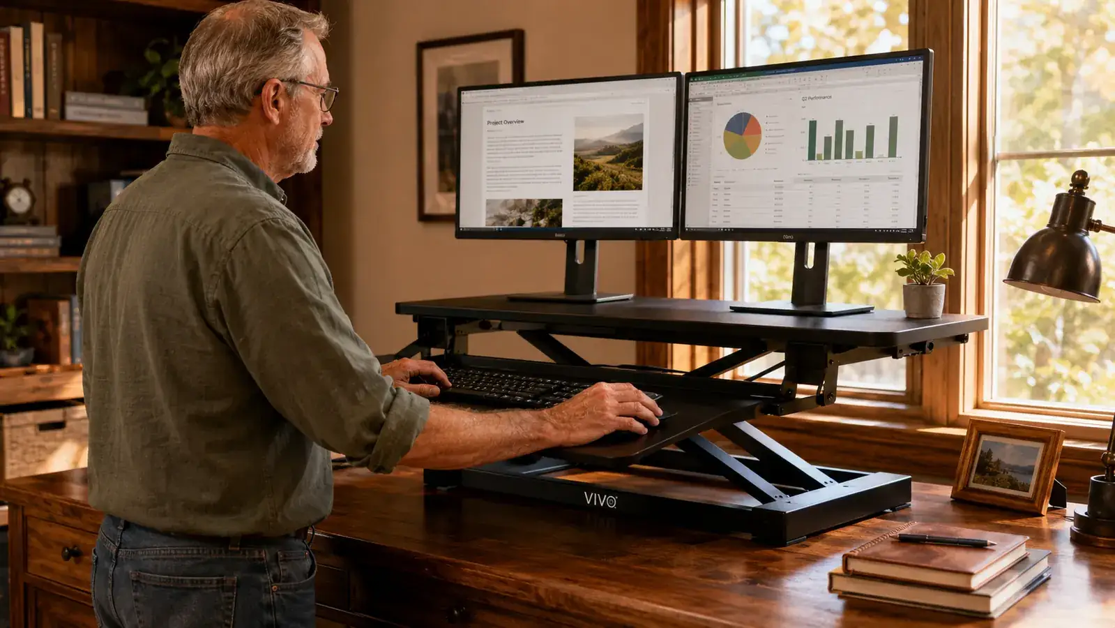 Hand pressing down on the edge of a raised desk converter to show slight forward tilt, monitors visible on top shelf